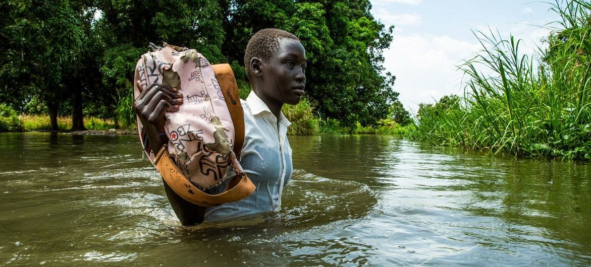 Una niña sostiene sus libros para que no se mojen de camino a casa desde la escuela en la aldea de Walangwalang, que se salvó de las inundaciones por el río, en las afueras de Juba, Sudán del Sur.